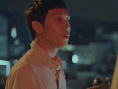 Jongwoo looking up in surprise, holding a can of beer in his hand, while on a rooftop. He starts smiling while talking.
