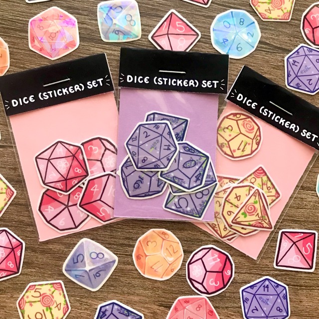 product photo of three sets of floral-themed dice stickers. These sets' themes include cherry blossoms, lavender, and roses. Individual sticker flakes from these sets are scattered around them. 