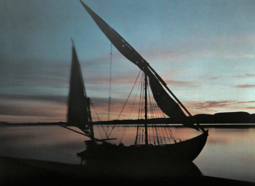 A boat sits still in the water at sunrise near Abu Simbel, Egypt, December 1923.Photograph by Jules 