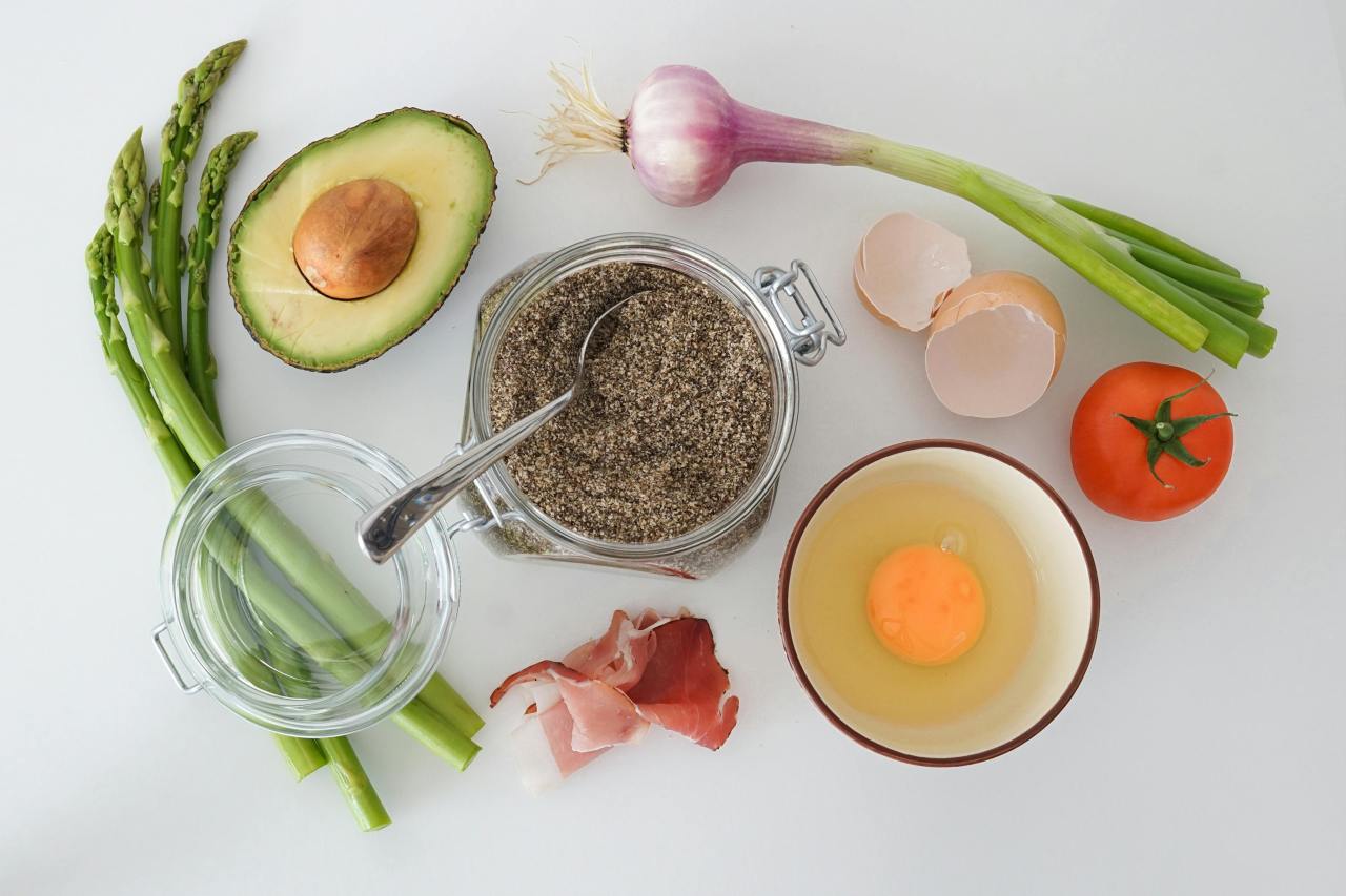 Ingredients including avocado, asparagus, egg, tomato, onion, and spices on a white surface.