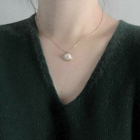 An image of a woman in a green v-neck sweater from the neck down with a gold necklace around their neck