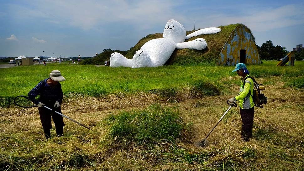 Landscapers trim grass in front of Dutch artist Florentijn Hofman’s 82-feet-high white rabbit, as it leans up against an old aircraft hangar as part of the Taoyuan Land Art Festival in Taoyuan, Taiwan (Photo by Wally Santana/AP via LA Times)