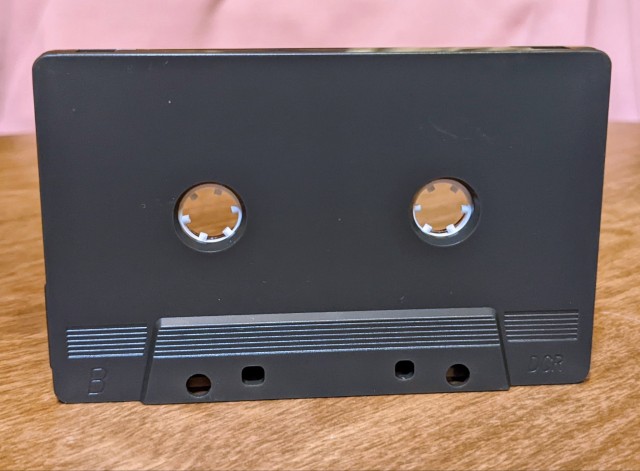Back of the cassette. This side of the shell is unlabeled, matte black, and windowless.