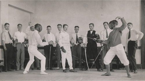 modernfencing:[ID: two men fencing foil, as men in suits stand in the background holding foils and s