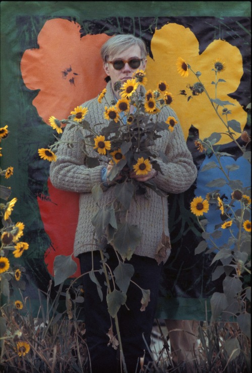 Andy Warhol in a field of black-eyed Susans holding a bouquet of flowers with an early “Flowers” can