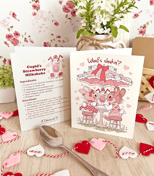 A photo of the front and back of a greeting card with art of two bunnies on a date with a milkshake shared between them. The back side features a recipe for a strawberry milkshake.