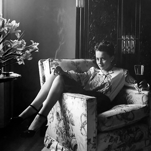    Actress, Olivia de Havilland relaxing at home with a cigarette and drink, Beverly