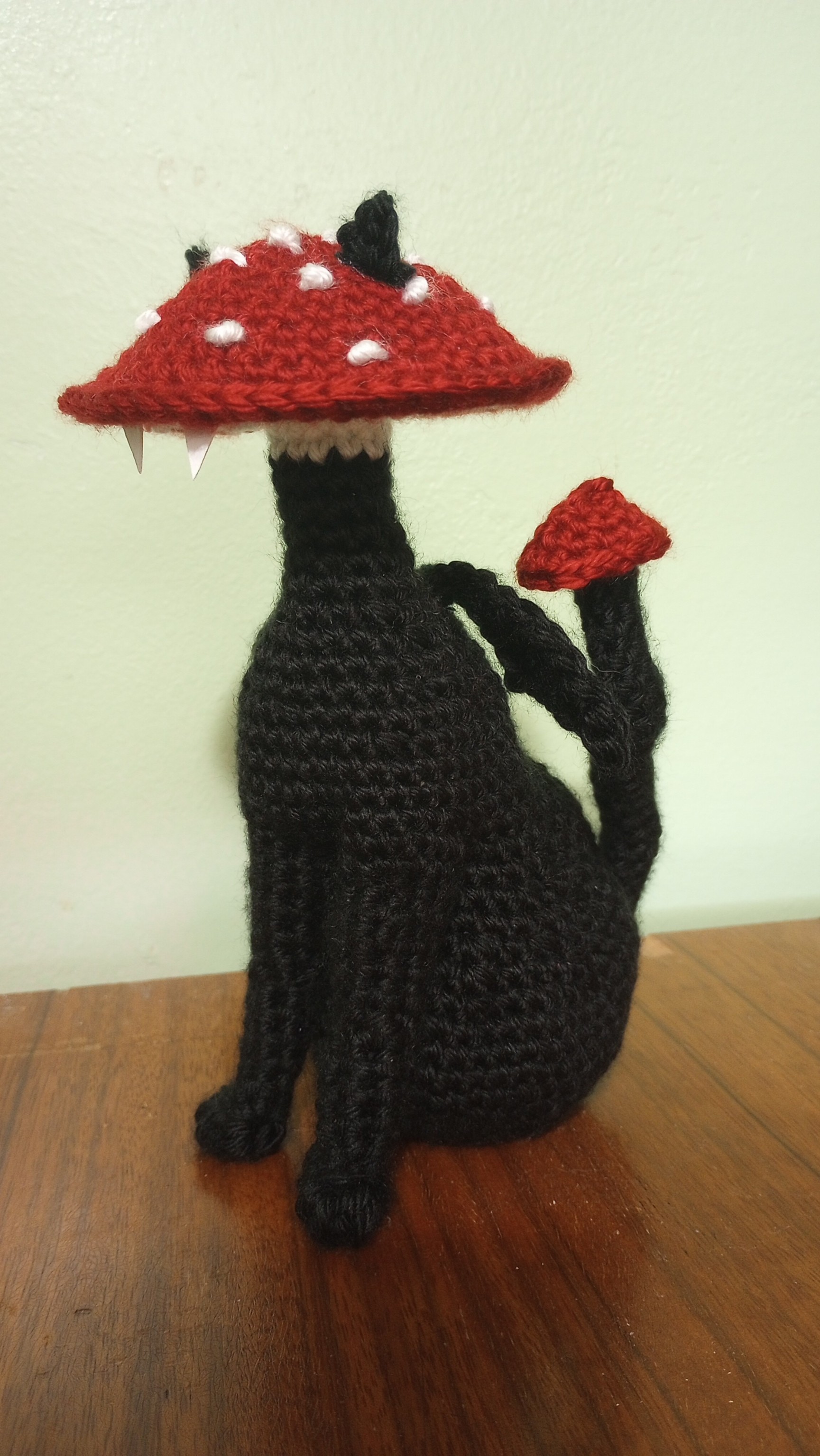 crocheted black cat with a red spotted mushroom for a head, side angle