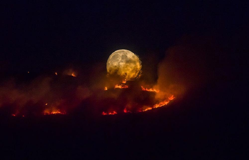 photos-of-space:  The full moon rises behind burning moorland near Stalybridge, England,