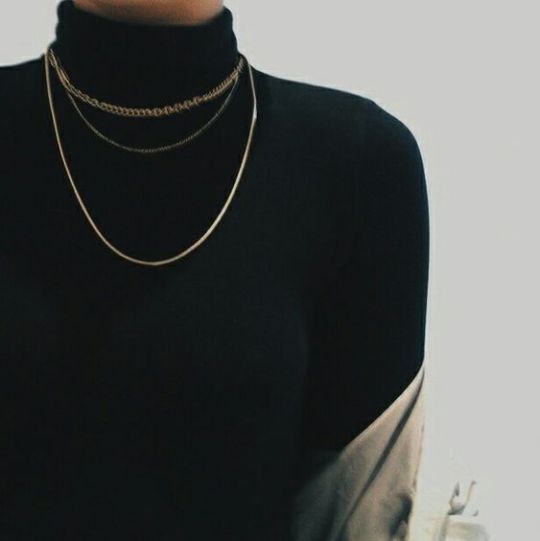 An image of a person wearing a black turtleneck with golden chains around the neck