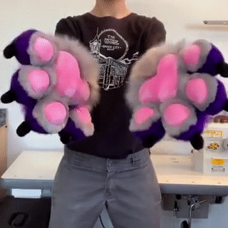 purple cuffs with grey paws and pink pawpads. the person wearing makes grabby hands at the camera