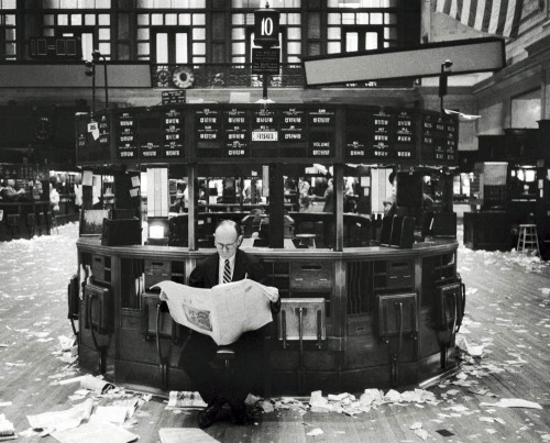 With trading debris all around him, a broker reads a newspaper in the New York Stock Exchange after 