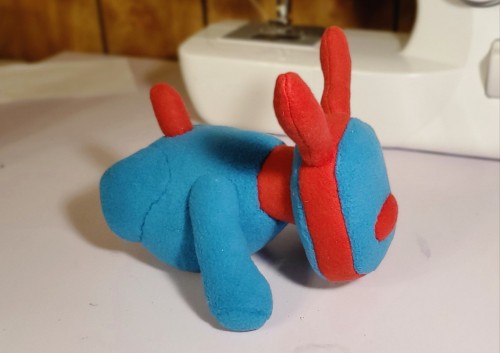 A photograph of a plush that is made to resemble an iDog. This one is blue and red, and facing the camera.