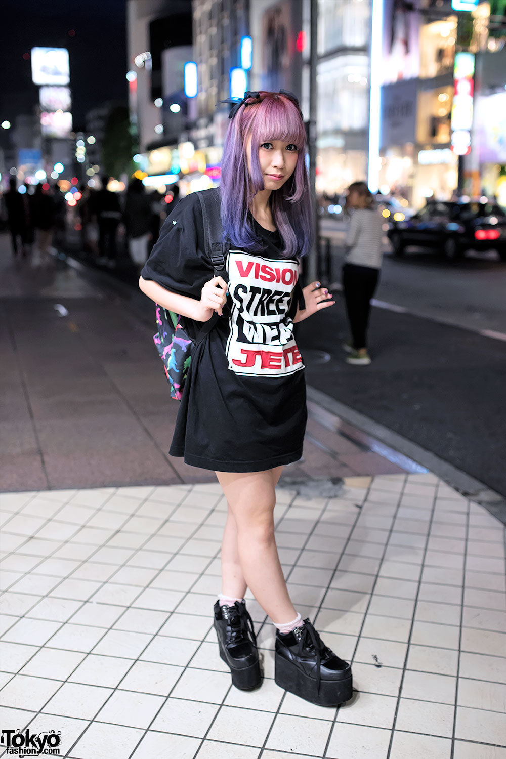 19-year-old Makocho on the street in Harajuku after dark with pretty pink-purple hair, a Vision Street Wear x Jouetie t-shirt dress, WEGO platforms, and a dinosaur backpack.