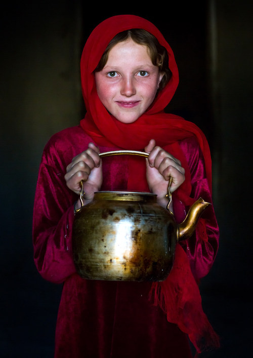 Portrait of an afghan girl with pale skin wearing red clothes and holding a tea pot, Badakhshan prov