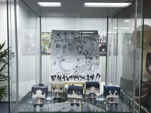 Hanamura Yaso, the author of the anime production manga, ANIMETA! (Animator!), shares photos of SnK Animation Director Asano Kyoji after meeting him at WIT Studio! Asano is posing in front of the merch display, which has plenty of SnK items.More on