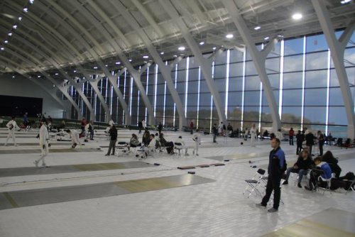 [ID: two photos of a fencing tournament, held in a second-story fieldhouse. Half of the indoor field