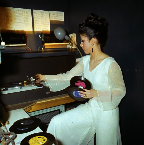 sixtiesgaragefuzzbeatpsychyeye:    A young female disc jockey or DJ changes a selection of records on twin turntables in a night club in 1967.  