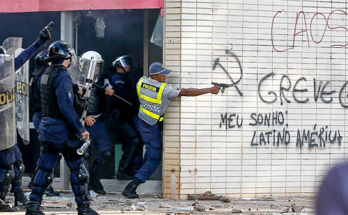 A police officer in Brasilia, Brazilfires shots at protesters while hiding behind a wall with a graf