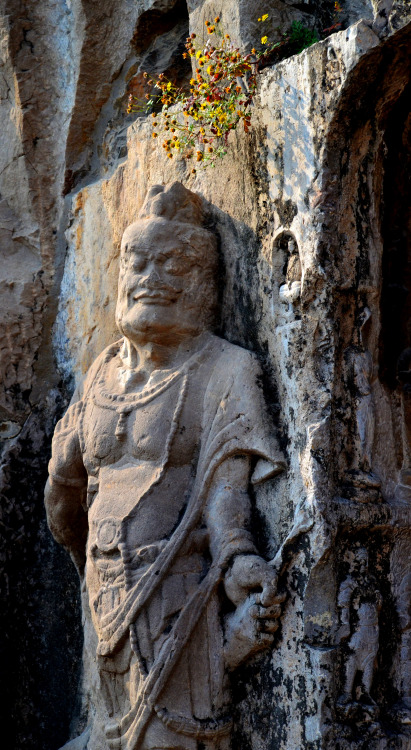 A stone relief statue with flowers over his head at the Longmen Grottoes UNESCO world heritage site,