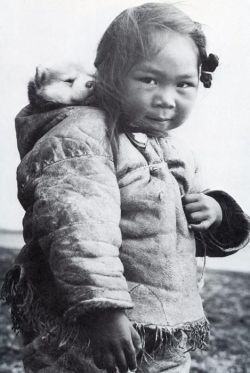 darksilenceinsuburbia: An Inuk girl with her husky puppy in the hood of her amatiuq circa 1920. Mothers would also carry their infants in the same manner. This little girl is playing mommy and baby with her puppy. 