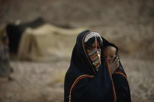 unrar:A Bedouin woman shields her child with her cloak, called an abaya, Palestine, Gordon Gahan.