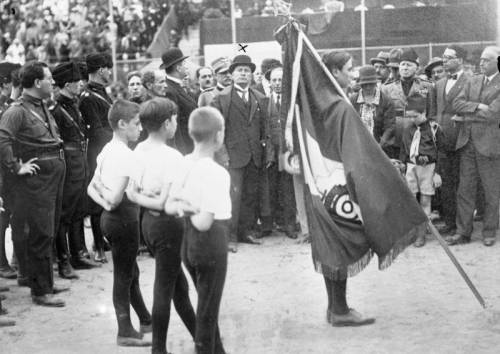 Children of a fascist youth organization consecrate a new flag, while Benito Mussolini looks on (Rom