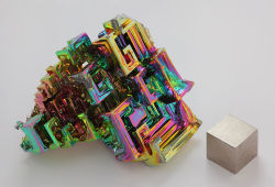 rhamphotheca:  An artificially grown bismuth crystal, illustrating the stairstep crystal structure, with a 1-cm cube of bismuth metal for comparison. The iridescent surface here is a very thin layer of oxidation. Photo: Heinrich Pniok                     