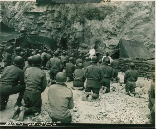 Stell helmeted American soldiers kneel in reverance at Easter morning services on the Italian Front.