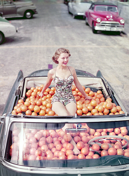 librar-y:Circa 1951. Swimsuit model in Cadillac convertible filled with oranges.