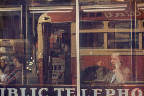 Man making a call from a public phone booth, seen in the reflection of a restaurant window, 1957.Pho