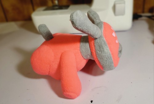 A photograph of a soft toy that is made to resemble an iDog. This one is pink and turned to the side, with pink hearts on the face.