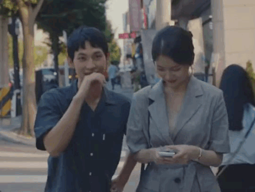 Jongwoo holding a hand to his mouth before ruffling his hair, the other hand on his hip, walking next to Jieun.
