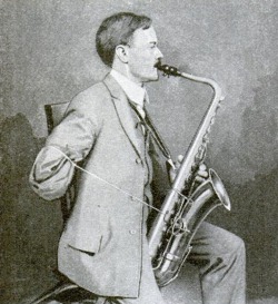 Musician using a device that enables him to play the saxophone with his left hand and a string tied to his crippled right arm, 1921.