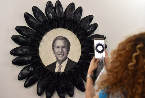 biladal-sham: A visitor takes a picture of George W. Bush surrounded by black shoes during the openi