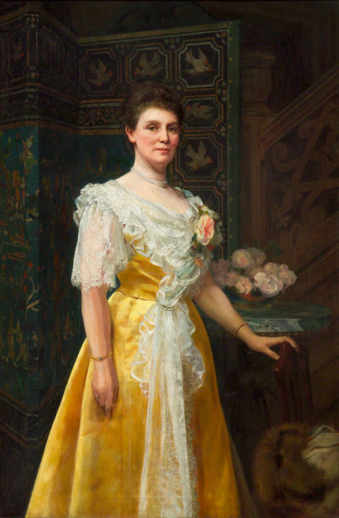 A portrait of a woman, standing three-quarter length, in a yellow dress, beside a bouquet of roses a