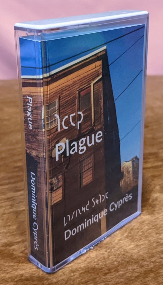 Front of Norelco cassette case for the album Plague by Dominique Cyprès, with the printed J-card visible. The cover image is a picture of a derelict building with a satellite dish against a blue sky.