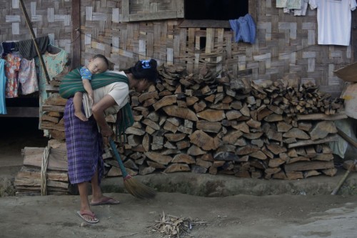 A woman with her child strapped to her back sweeps at the Janmai Kaung KBC Internally Displaced Pers