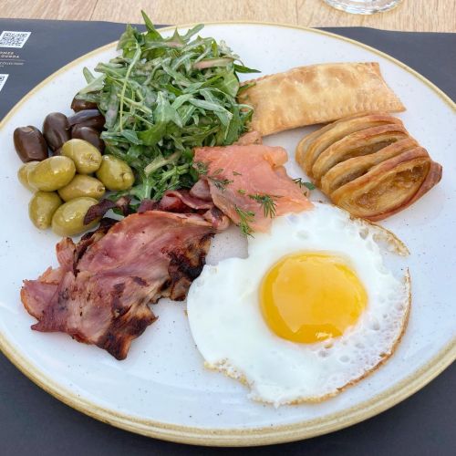 Breakfast buffet with fried egg, bacon, cured salmon, olives, arugula salad, apple pastry, cheese pi