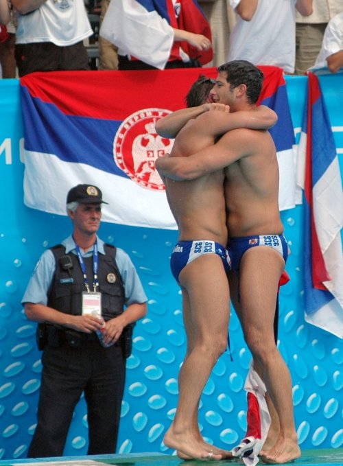 A couple of straight swimmers hugging each other tightly so their speedo bulges are touching.