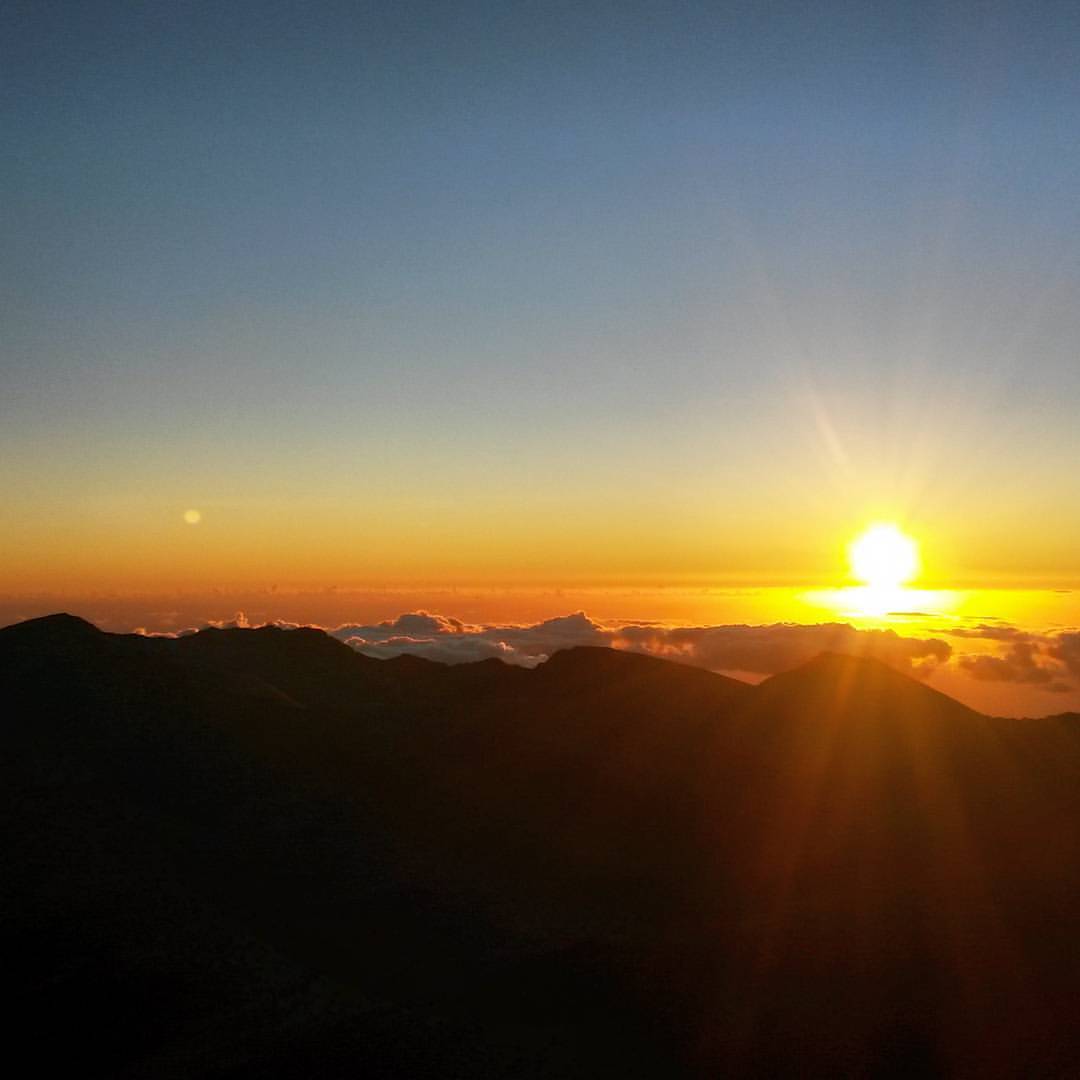 Sunrise breaking through the cloud cover over the ocean at Haleakala summit in Hawaii.