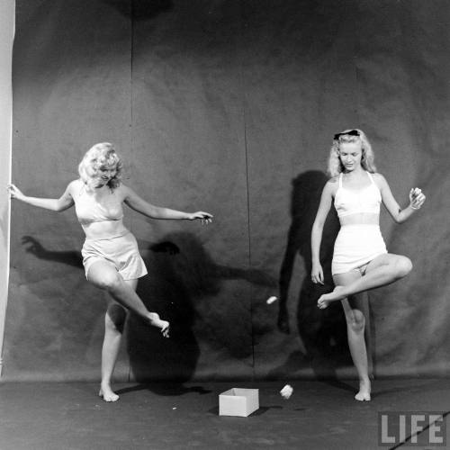 Two women trying to toss paper into box using only their feet(Fritz Goro. 1942)