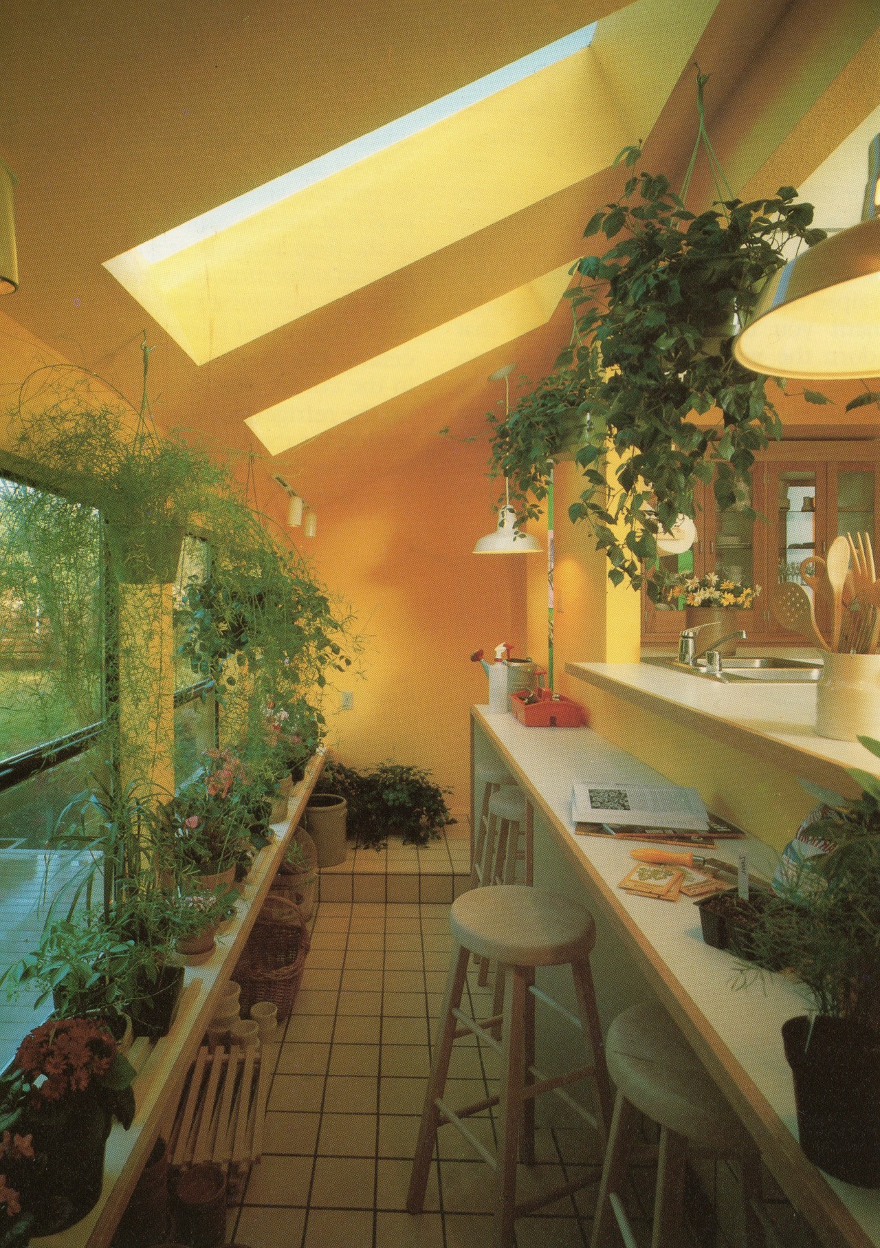 For the avid gardener, a conservatory off the kitchen area makes a lot of sense. Close to water and wash-up materials, a long narrow alcove such as this one lets you fuss with plants while keeping an eye on preparing the meals.Beyond The Kitchen: A Dreamer’s Guide, 1985 #vintage#vintage interior#1980s#interior design#home decor#conservatory#kitchen#house plants#stools#countertop#yellow#wall paint#skylight#contemporary#style#home#architecture#pendant lamp