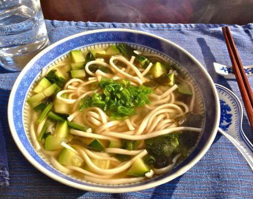 Steaming bowl of good udon noodles in miso soup with wakame seaweed, zucchini, spinach, topped with 