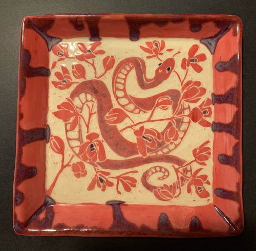 a large square ceramic tray. it's red, pink and purple. it's decorated with a snake twined through a few branches of orchids and the rim is a drippy purple