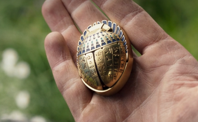 Tacky gold scarab resting on the palm of a hand. It had lapis lazuli details, and hieroglyphs that mirror each other on either side of the body. The hieroglyphs say nothing as it is not proper Egyptian.