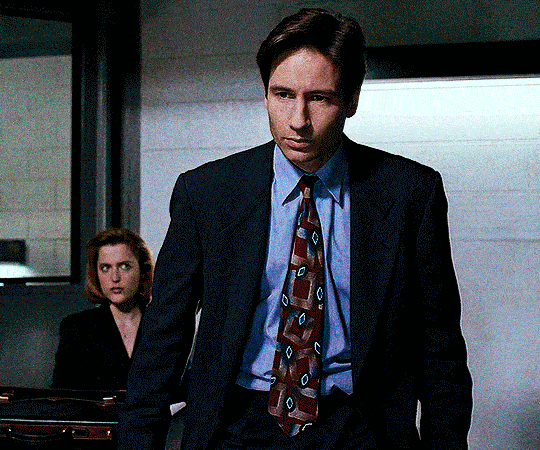 gif 4 of 6. Mulder gets up from a table he was sitting on and gets closer to where Boggs is sitting down. the convict is sweaty and exhausted, without strenght to even lift his head. Mulder crouches so we can be in Boggs' eye level.
