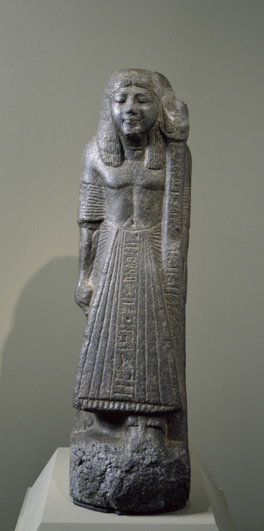 Ancient Egyptian granodiorite statue of a man named Hor-nakht, holding the standard of a ram-headed 