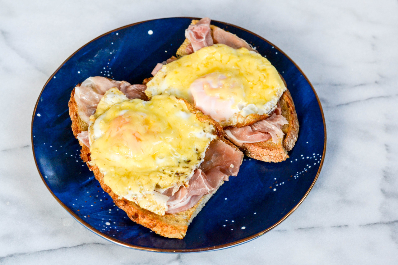 Picture of uitsmijter, a n open-face sandwich of ham, egg, and cheese, on a blue plate on a marble slab, an overhead shot