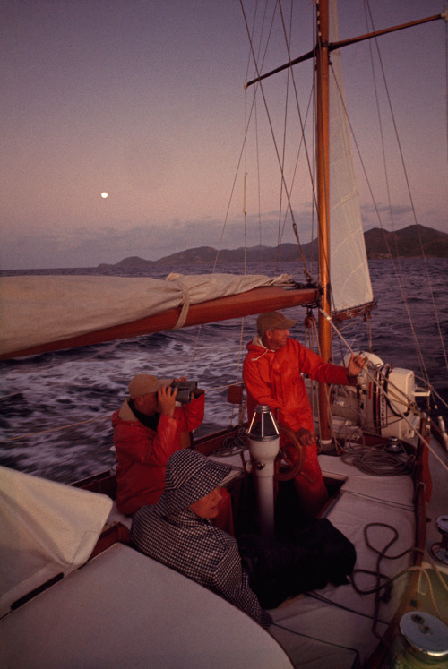 Sailors wearing raingear sit in a sailboat&rsquo;s cockpit awaiting dawn in the West Indies, Oct
